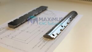 Precyzyjnie frezowane metalowe prowadnice (szyny) z otworami, leżące na rysunku technicznym.