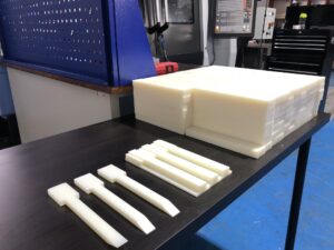 Stos surowego tworzywa konstrukcyjnego (PEEK:POM) i obrobione, frezowane elementy plastikowe. Obróbka tworzyw sztucznych.